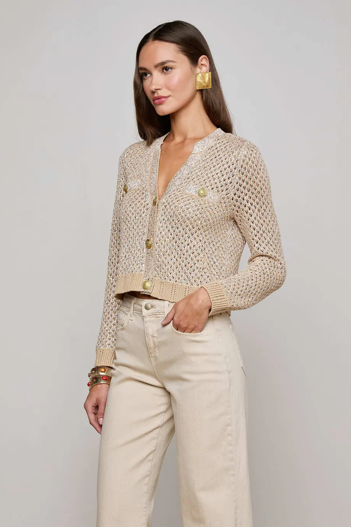 Woman wearing a beige knitted cardigan and light-colored pants against a plain background