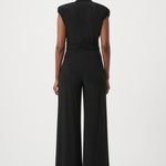 A model viewed from the back wearing a black sleeveless jumpsuit with a gathered waist and wide legs, set against a plain light gray studio background.