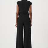 A model viewed from the back wearing a black sleeveless jumpsuit with a gathered waist and wide legs, set against a plain light gray studio background.