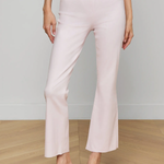 Person wearing light pink pants with a white belt and clear high-heeled sandals on a wooden floor.