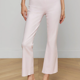 Person wearing light pink pants with a white belt and clear high-heeled sandals on a wooden floor.
