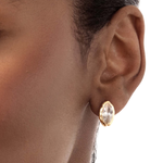 A close-up of a model's ear wearing a small gold stud earring with a marquise-cut clear gemstone.