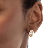 A close-up of a model's ear wearing a small gold stud earring with a marquise-cut clear gemstone.