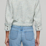 Person wearing a patterned jacket and light blue jeans on a plain background