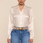 Woman wearing a white satin shirt and blue jeans against a beige background