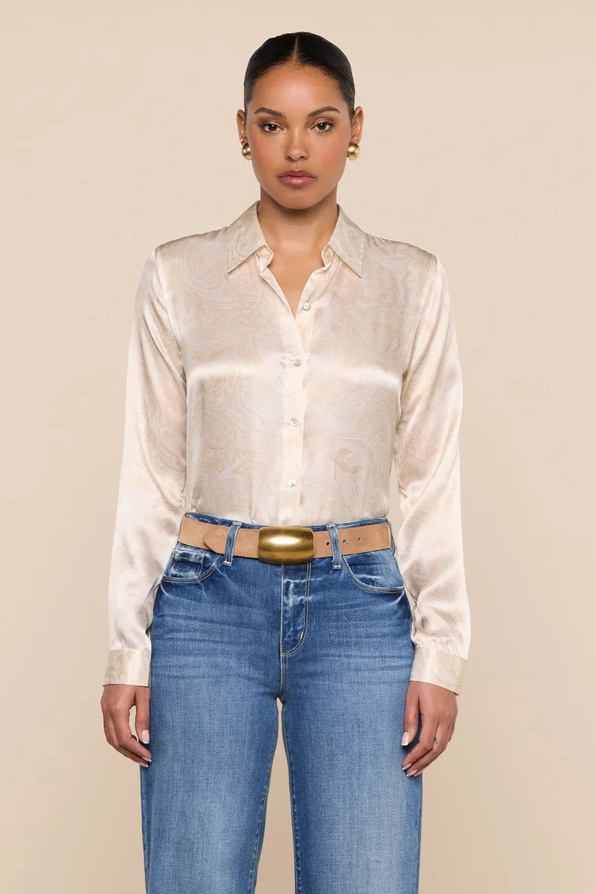 Woman wearing a white satin shirt and blue jeans against a beige background