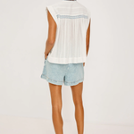 Woman wearing a white sleeveless top and light blue denim shorts on a plain background
