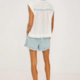 Woman wearing a white sleeveless top and light blue denim shorts on a plain background