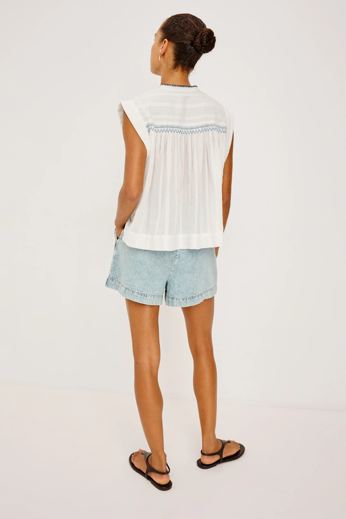 Woman wearing a white sleeveless top and light blue denim shorts on a plain background