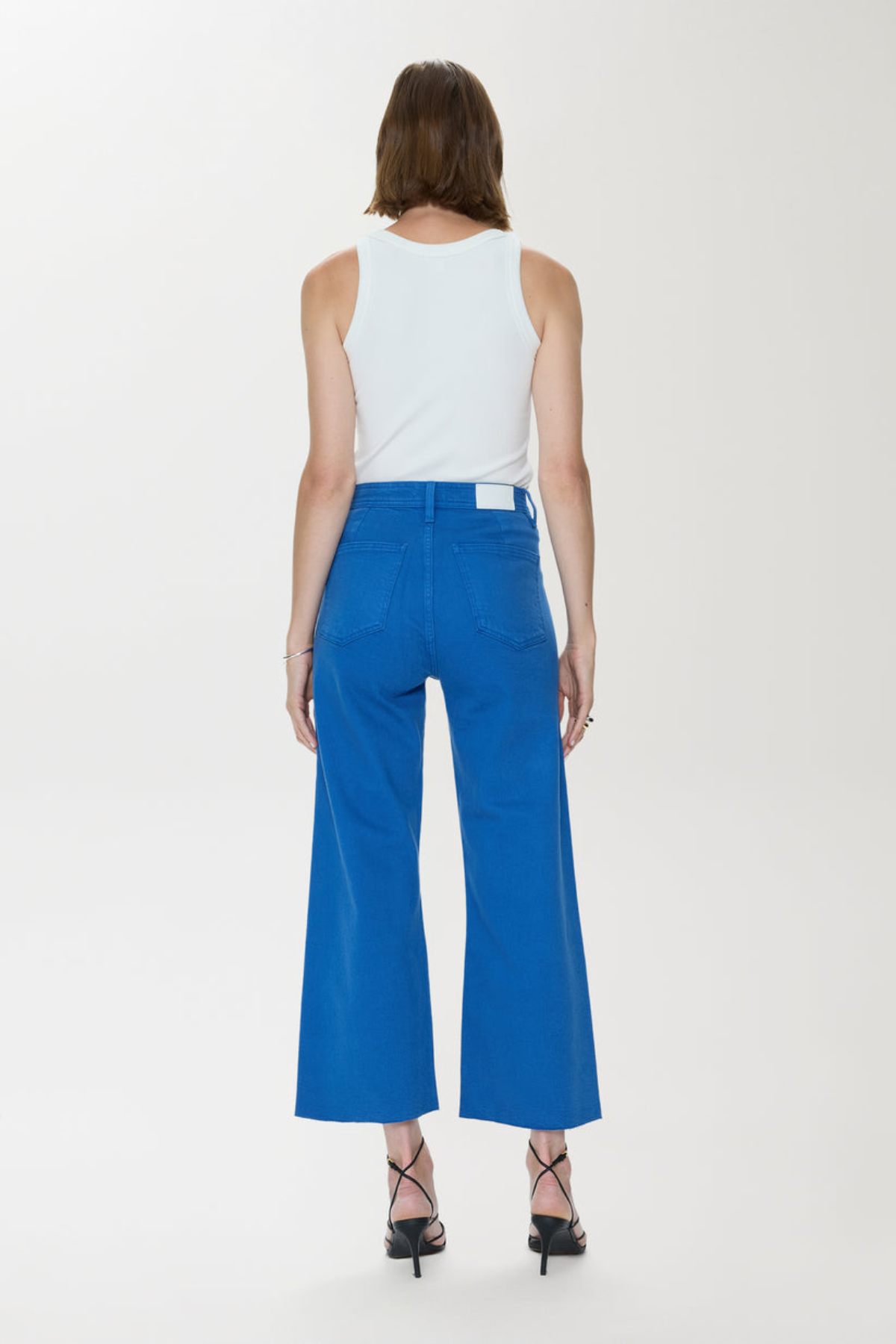 Person wearing a white sleeveless top and blue high-waisted pants on a white background