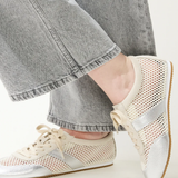 Close-up of feet wearing beige sneakers with silver accents and gray jeans.