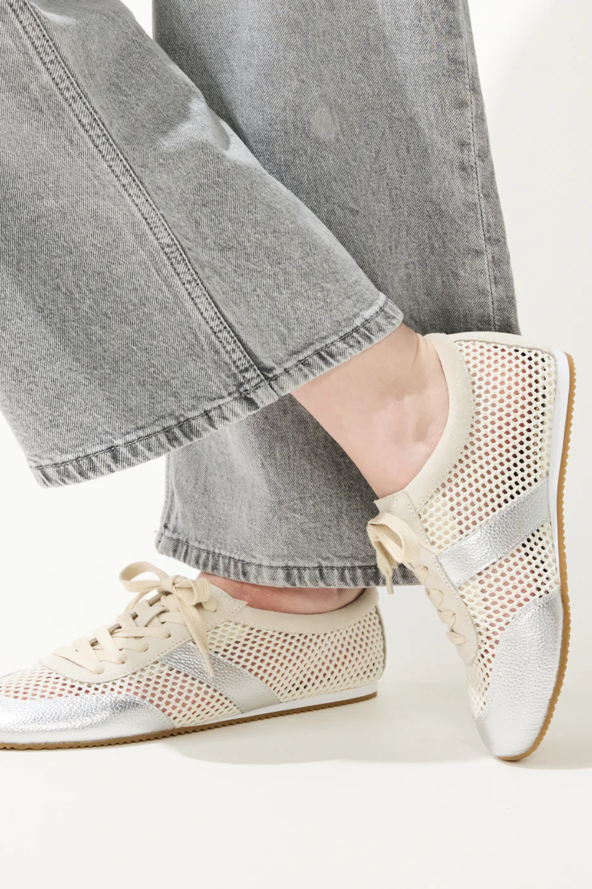Close-up of feet wearing beige sneakers with silver accents and gray jeans.
