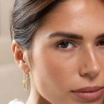 A close-up of a woman wearing a delicate gold huggie hoop earring with a textured, woven-like design.