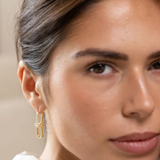 A close-up of a woman wearing a delicate gold huggie hoop earring with a textured, woven-like design.