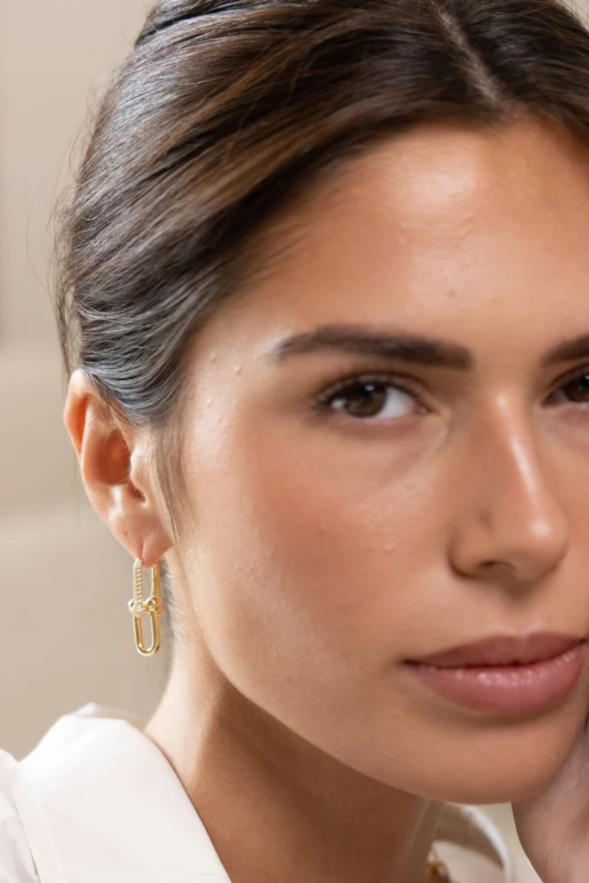 A close-up of a woman wearing a delicate gold huggie hoop earring with a textured, woven-like design.