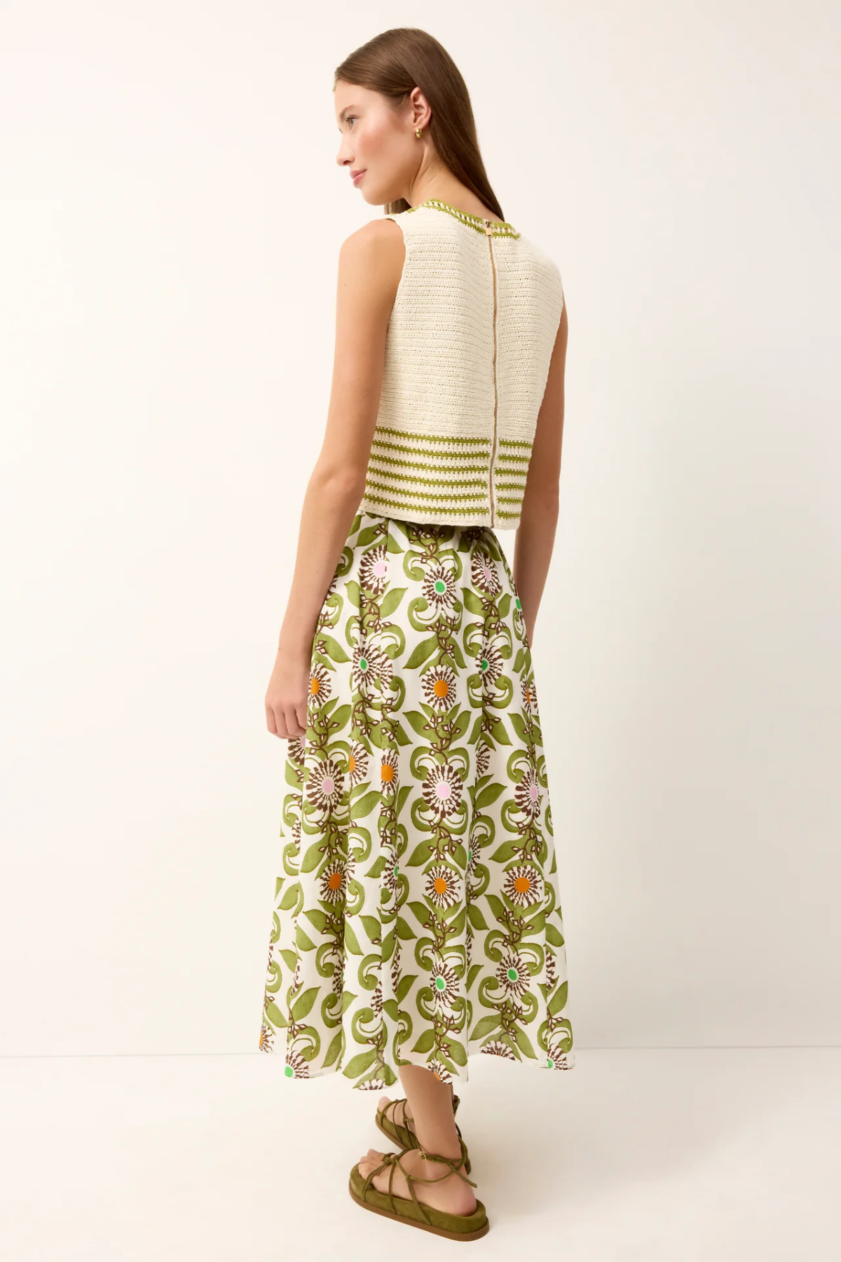 Woman wearing a white sleeveless top with green stripes and a green floral skirt on a white background