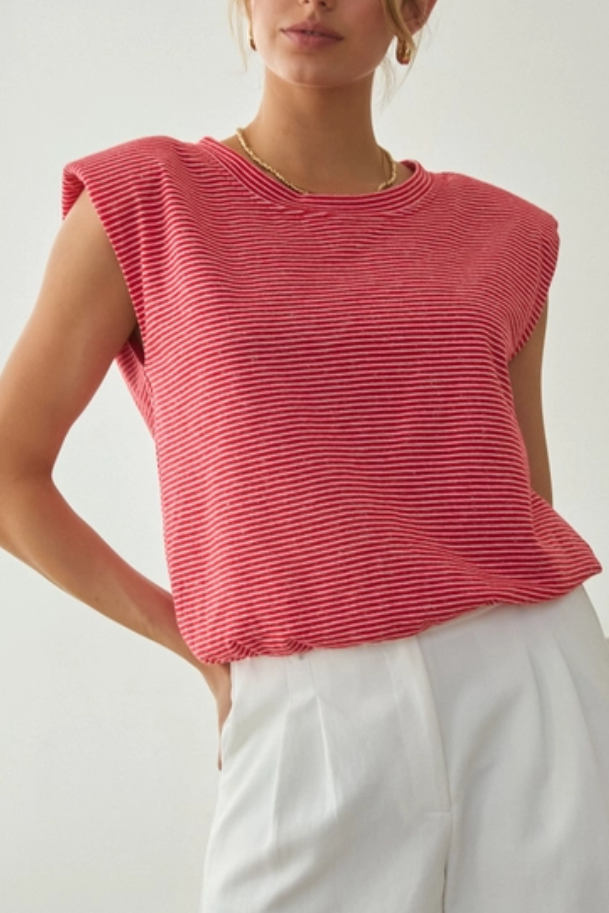 Woman wearing a red striped sleeveless top and white pants on a light background