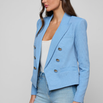 Woman wearing a light blue blazer over a white top and jeans on a plain background