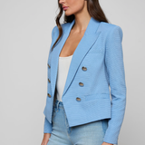 Woman wearing a light blue blazer over a white top and jeans on a plain background