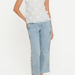 Woman wearing a white sleeveless top with floral details and light blue jeans on a white background