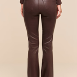 Rear view of a model wearing dark brown faux-leather flare pants with a matching belt, paired with a dark brown ribbed long-sleeve top, against a solid beige background.