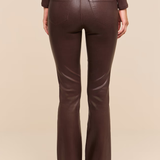 Rear view of a model wearing dark brown faux-leather flare pants with a matching belt, paired with a dark brown ribbed long-sleeve top, against a solid beige background.