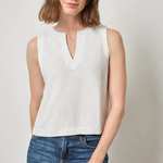 Woman wearing a white sleeveless top and blue jeans against a plain background