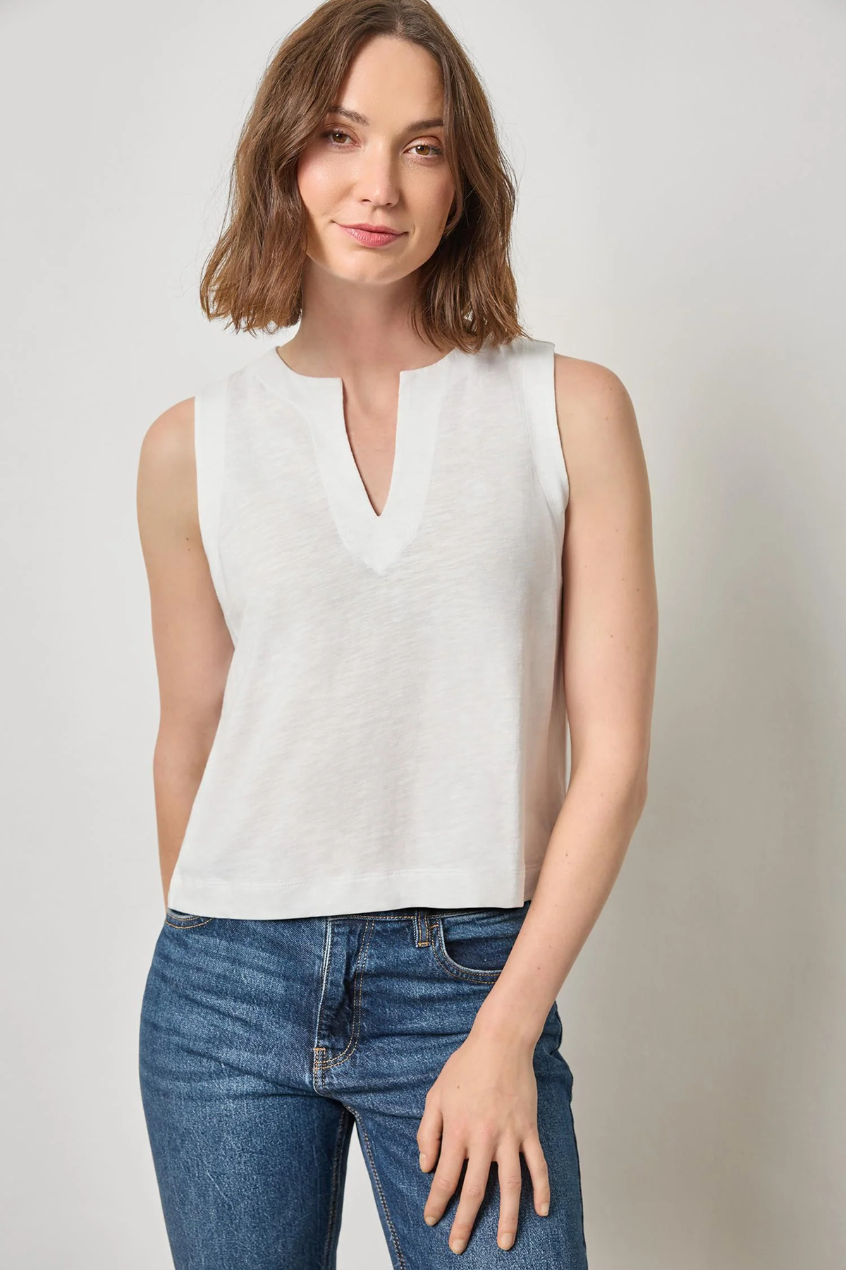Woman wearing a white sleeveless top and blue jeans against a plain background