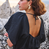 Woman in a black dress with an open back standing against a rocky landscape.