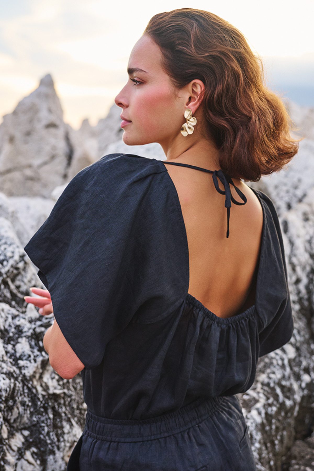 Woman in a black dress with an open back standing against a rocky landscape.