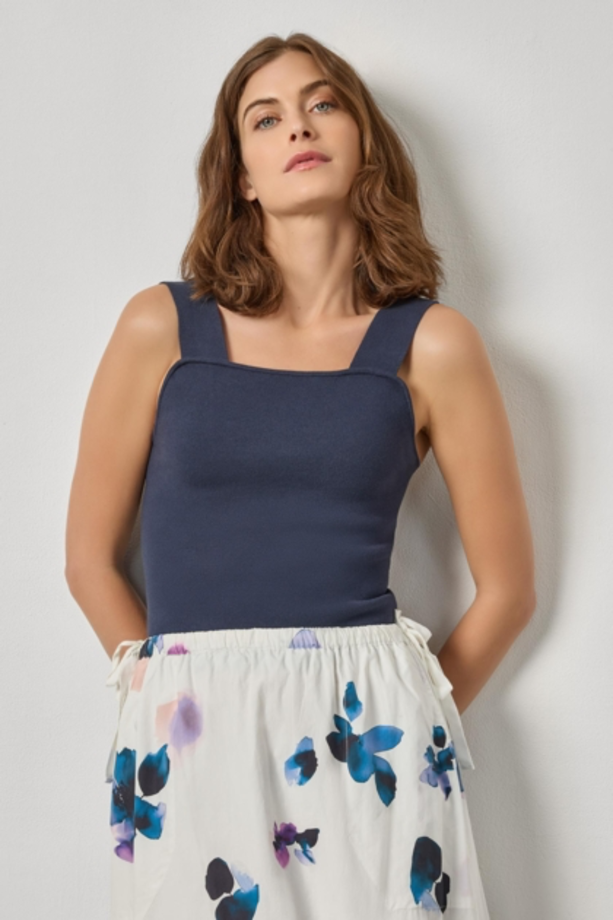 Woman wearing a navy tank top and floral skirt against a plain background