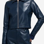 A woman wearing a shiny navy faux-leather cropped jacket with a front zipper and matching navy shorts, shown against a light gray studio background.