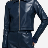 A woman wearing a shiny navy faux-leather cropped jacket with a front zipper and matching navy shorts, shown against a light gray studio background.