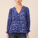 Woman wearing a blue patterned blouse and dark jeans on a beige background