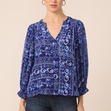 Woman wearing a blue patterned blouse and dark jeans on a beige background