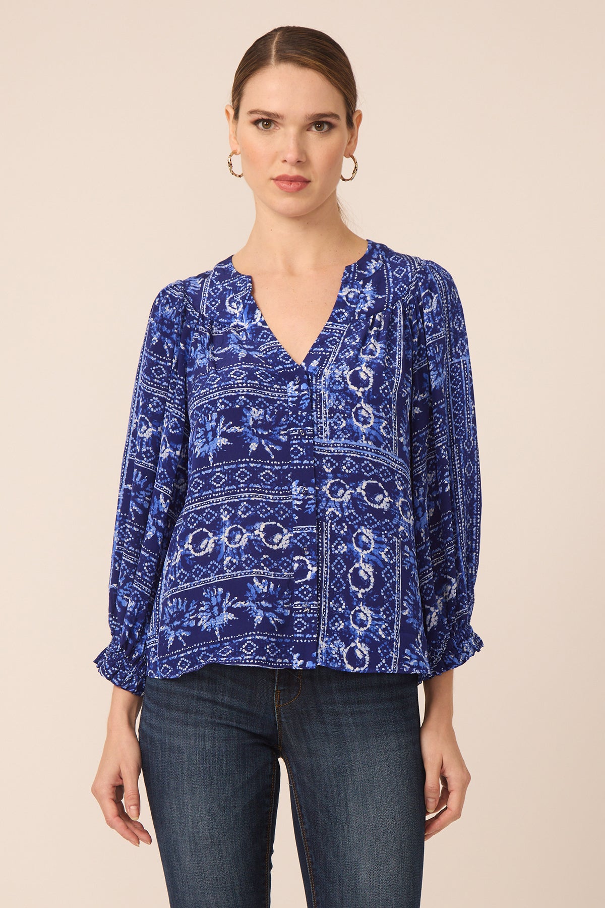 Woman wearing a blue patterned blouse and dark jeans on a beige background