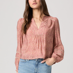 Woman wearing a pink floral blouse and blue jeans on a light gray background