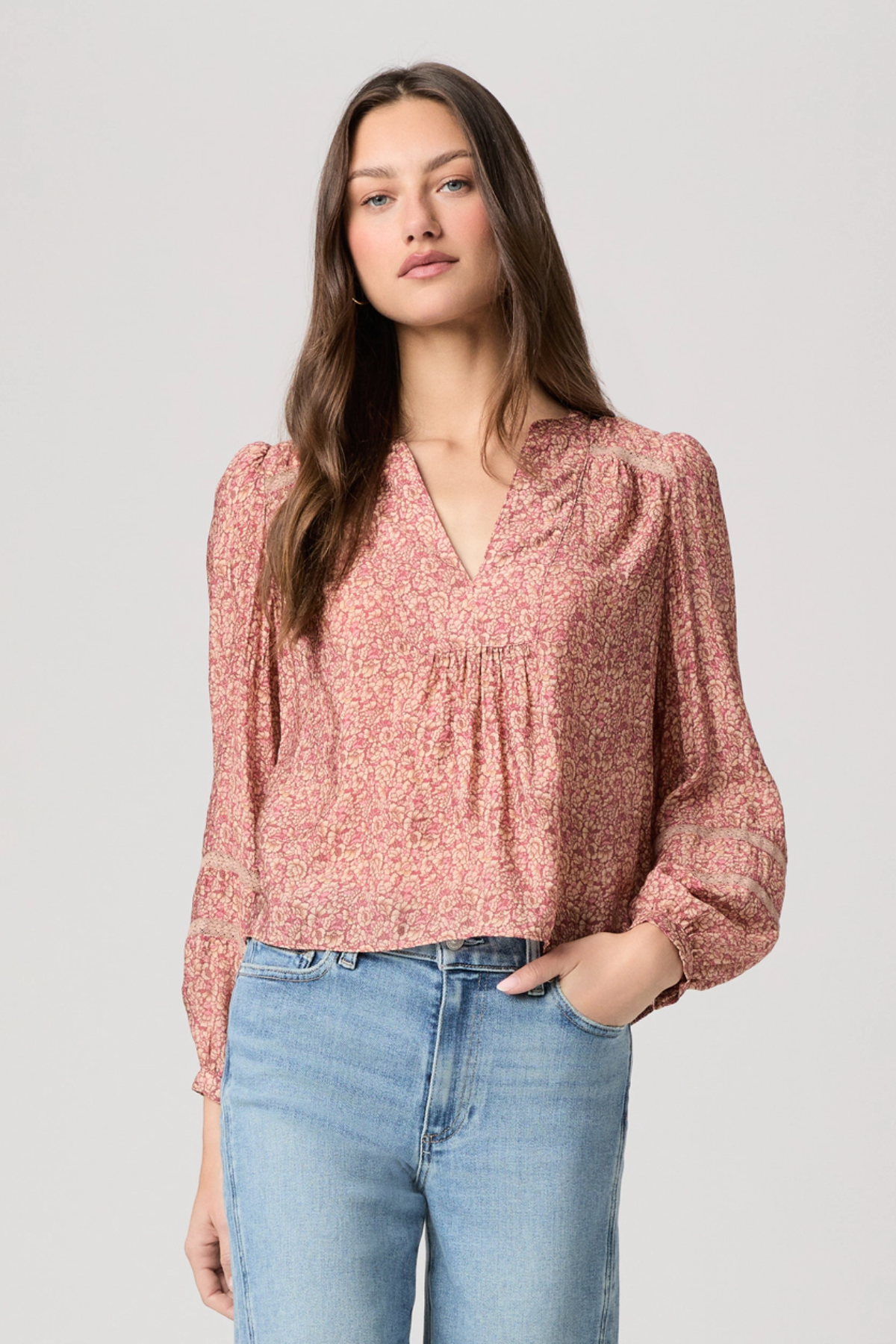 Woman wearing a pink floral blouse and blue jeans on a light gray background