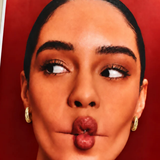 A close-up portrait of a woman with dark hair pulled back, wearing small gold hoop earrings, against a solid red background.