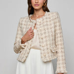 Woman wearing a textured beige jacket over a white top and skirt on a gray background