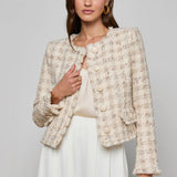 Woman wearing a textured beige jacket over a white top and skirt on a gray background