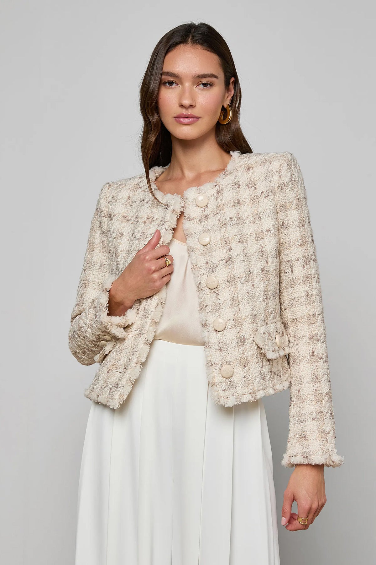 Woman wearing a textured beige jacket over a white top and skirt on a gray background