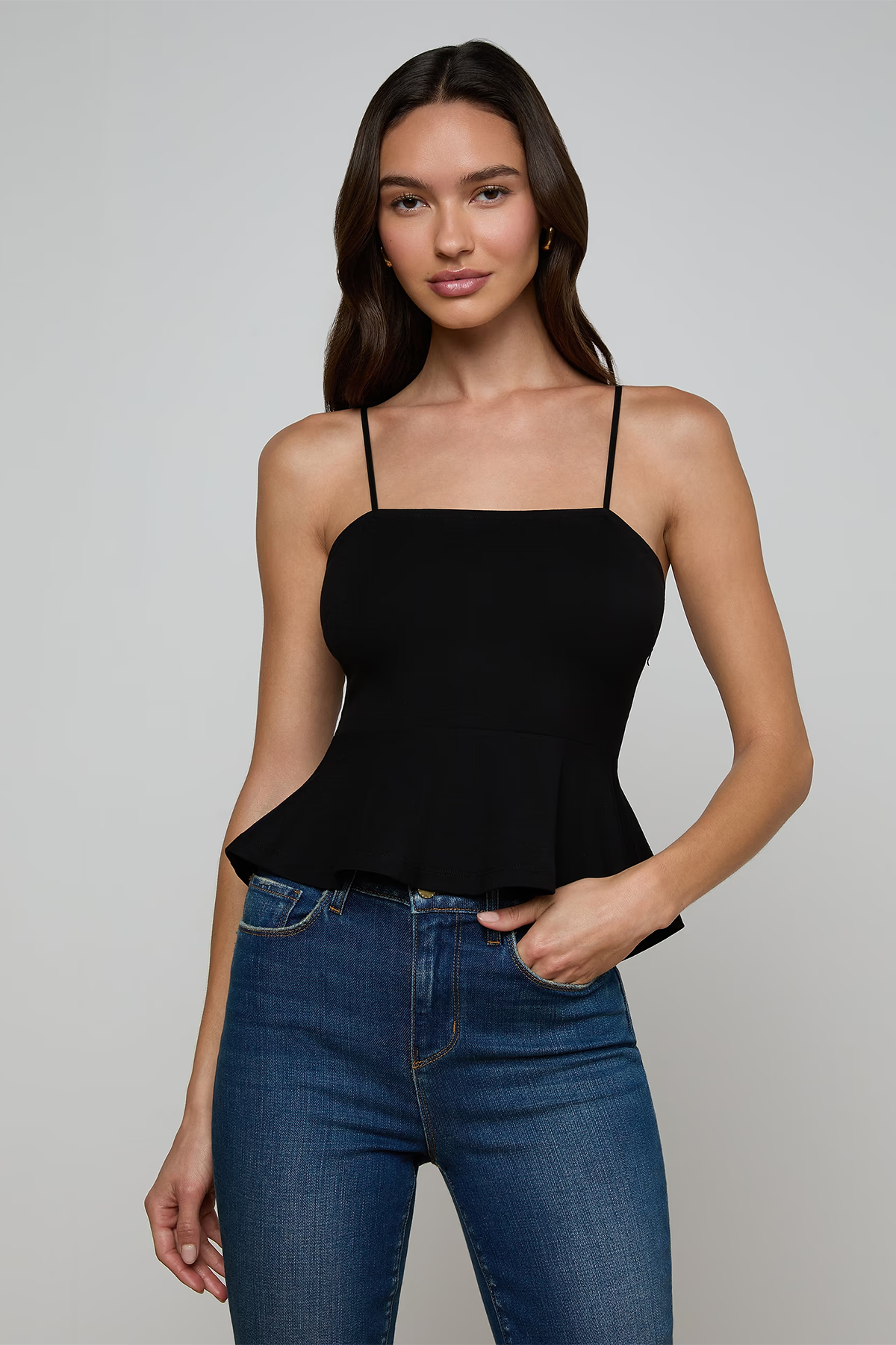 Woman wearing a black peplum top and blue jeans against a gray background