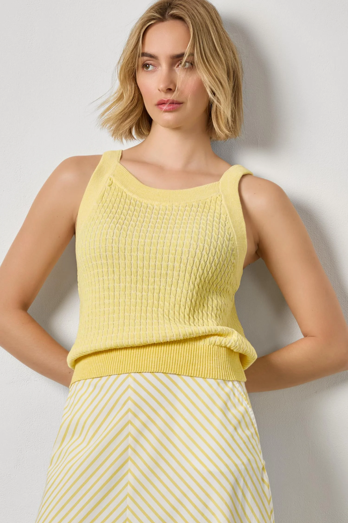 Woman wearing a yellow sleeveless top and skirt against a plain background
