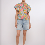 Woman wearing a colorful floral top and denim shorts on a white background