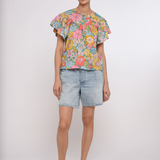 Woman wearing a colorful floral top and denim shorts on a white background