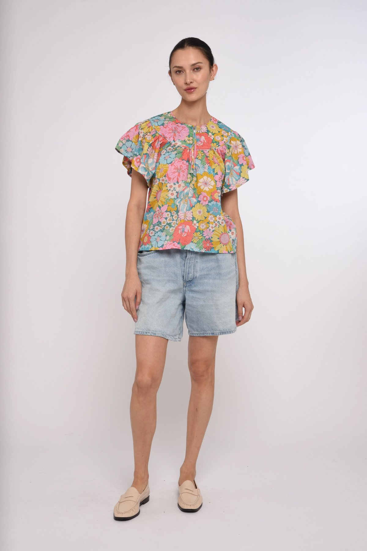 Woman wearing a colorful floral top and denim shorts on a white background