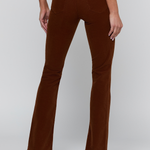Rear view of a model wearing brown corduroy flare pants and black high heels against a light gray studio background.