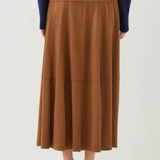 A model is shown from the back wearing a brown pleated midi skirt, a navy blue long-sleeve top, and black heeled sandals against a plain white studio background.