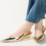 Gold pointed-toe shoes worn with blue jeans on a light background